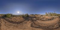 a wide lensed image of some dirt hills and bushes as well as the sun