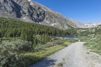 a trail is on the side of some large mountains with trees and snow capped peaks