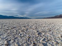 large vast expanse with white sand in the foreground with blue sky above it and distant mountains in the background