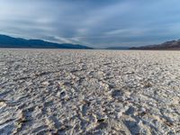 large vast expanse with white sand in the foreground with blue sky above it and distant mountains in the background