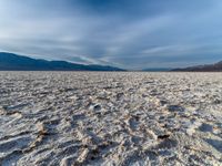 large vast expanse with white sand in the foreground with blue sky above it and distant mountains in the background