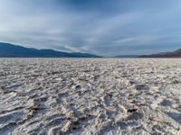 large vast expanse with white sand in the foreground with blue sky above it and distant mountains in the background