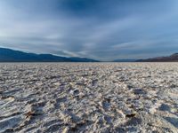 large vast expanse with white sand in the foreground with blue sky above it and distant mountains in the background