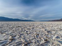 large vast expanse with white sand in the foreground with blue sky above it and distant mountains in the background