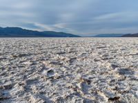 large vast expanse with white sand in the foreground with blue sky above it and distant mountains in the background