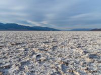 large vast expanse with white sand in the foreground with blue sky above it and distant mountains in the background