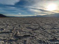 the sun peeking over the mountains behind a sandy area with very no grass or water