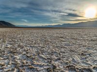 the sun peeking over the mountains behind a sandy area with very no grass or water