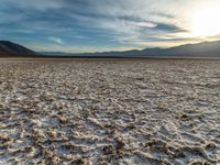 the sun peeking over the mountains behind a sandy area with very no grass or water