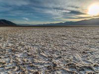 the sun peeking over the mountains behind a sandy area with very no grass or water