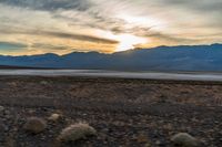 the sun sets behind mountains in a desert landscape with green grass and scrubby weeds