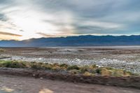 the sun sets behind mountains in a desert landscape with green grass and scrubby weeds