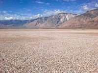 an empty desert with rocky ground, mountains in the distance and clouds in the sky