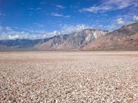 an empty desert with rocky ground, mountains in the distance and clouds in the sky