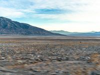 a desert with a lone yellow van on it's side, and large mountains in the background