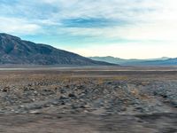 a desert with a lone yellow van on it's side, and large mountains in the background