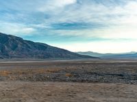 a desert with a lone yellow van on it's side, and large mountains in the background