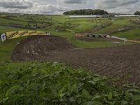 a dirt bike race with a grassy hill in the background and spectators on the side of the course