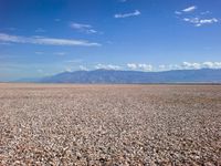 an empty beach and mountains with gravel on the foreground under blue skies and clouds