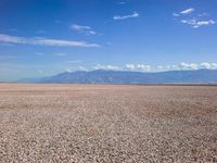 an empty beach and mountains with gravel on the foreground under blue skies and clouds