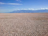 an empty beach and mountains with gravel on the foreground under blue skies and clouds