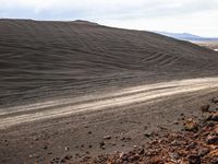 a large mound of dirt with many tracks in it and mountains in the background in the middle