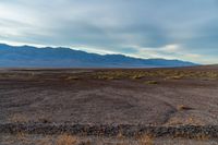 an empty field with mountains in the distance in a cloudy sky near a rocky beach