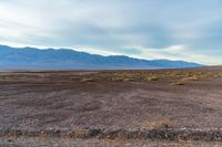 an empty field with mountains in the distance in a cloudy sky near a rocky beach