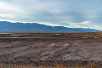 an empty field with mountains in the distance in a cloudy sky near a rocky beach