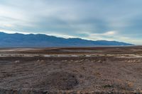 an empty field with mountains in the distance in a cloudy sky near a rocky beach