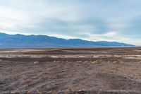 an empty field with mountains in the distance in a cloudy sky near a rocky beach