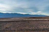 an empty field with mountains in the distance in a cloudy sky near a rocky beach