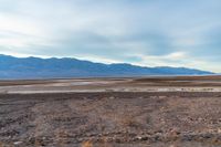 an empty field with mountains in the distance in a cloudy sky near a rocky beach