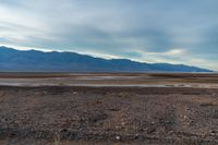 an empty field with mountains in the distance in a cloudy sky near a rocky beach