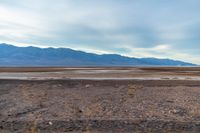 an empty field with mountains in the distance in a cloudy sky near a rocky beach