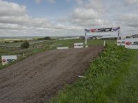 a dirt track is shown on a cloudy day with clouds overhead and a sign saying bsb