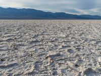 a white desert has many patches of dirt on it as a person in the distance looks at them