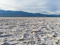 a white desert has many patches of dirt on it as a person in the distance looks at them