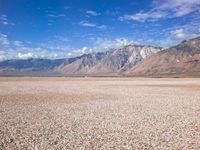 an area with very flat land covered in gravel and rocks with mountains in the background