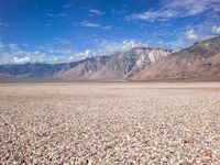 an area with very flat land covered in gravel and rocks with mountains in the background