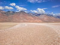 a vast open desert land filled with hills and boulders under blue skies and clouds in the background