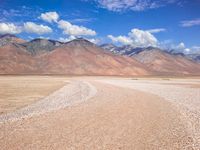 a vast open desert land filled with hills and boulders under blue skies and clouds in the background