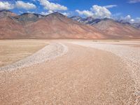 a vast open desert land filled with hills and boulders under blue skies and clouds in the background