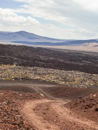 there is a dirt path that runs through the desert with mountains in the background and snow in the sky