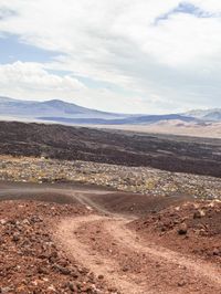 there is a dirt path that runs through the desert with mountains in the background and snow in the sky