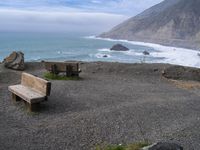 wooden benches sitting on a rock near the ocean and rocky cliff slopes near the shore