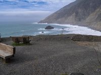 wooden benches sitting on a rock near the ocean and rocky cliff slopes near the shore