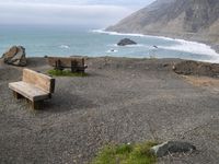 wooden benches sitting on a rock near the ocean and rocky cliff slopes near the shore