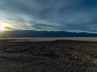 an empty dirt field with a fire hydrant near it and some mountains under a cloudy sky