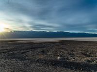 an empty dirt field with a fire hydrant near it and some mountains under a cloudy sky